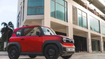 Mobil listrik kompak VinFast VF 3 berwarna merah cerah terparkir di depan gedung modern.