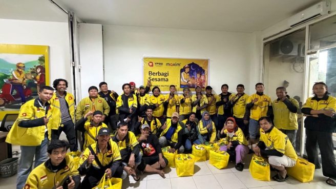 Sekelompok mitra pengemudi Maxim mengenakan jaket kuning ikonik berpose bersama di dalam ruangan kantor cabang. Di depan mereka terdapat tas belanja besar berwarna kuning berisi paket sembako. Di latar belakang terdapat banner bertuliskan 'YPSSI Maxim - Berbagi Sesama Menyalurkan Sembako dan BHR Ramadan'.