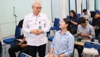 Sekretaris Jenderal Kemnaker, Cris Kuntadi, mengenakan seragam putih SIAPkerja sedang berbincang dengan seorang pencari kerja wanita berbaju biru muda dalam acara Walk-In Interview di Gedung Pusat Pasar Kerja. Di latar belakang, terlihat beberapa pencari kerja lainnya sedang duduk menunggu giliran wawancara.
