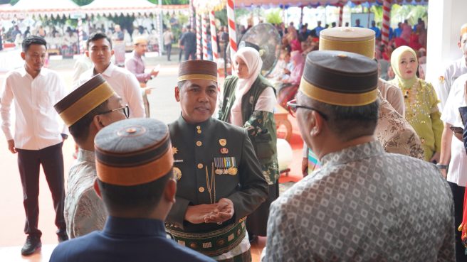 Bupati Wajo Andi Rosman mengenakan Jas Tutup hijau tua beradu argumen santai dengan pejabat lain di sela acara Hari Jadi Bone, mengenakan Songkok Recca dan sarung sutra Lipa Sabbe.