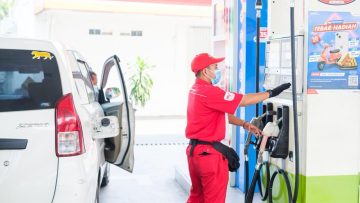 Operator SPBU Pertamina dengan seragam merah dan masker melakukan pengawasan ketat saat mengisi BBM subsidi ke mobil konsumen di Situbondo.
